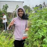 Beatrice holding bag of cherry tomatoes and a peace sign in garden